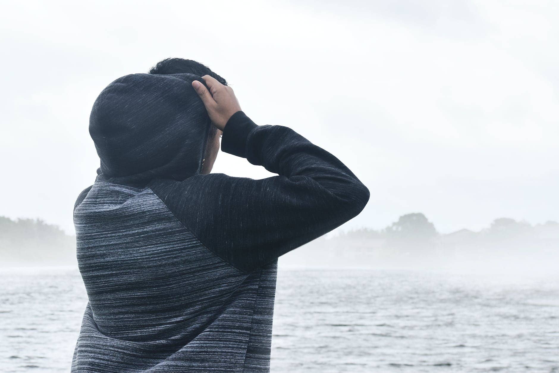 person in black and grey raglan hoodie near body of water
